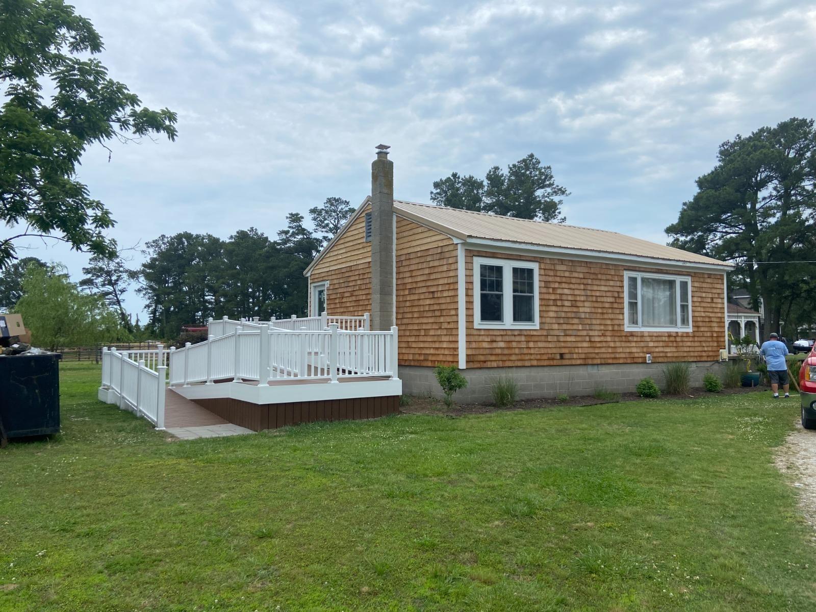 A single-story house with light wood siding and a white deck on the side
